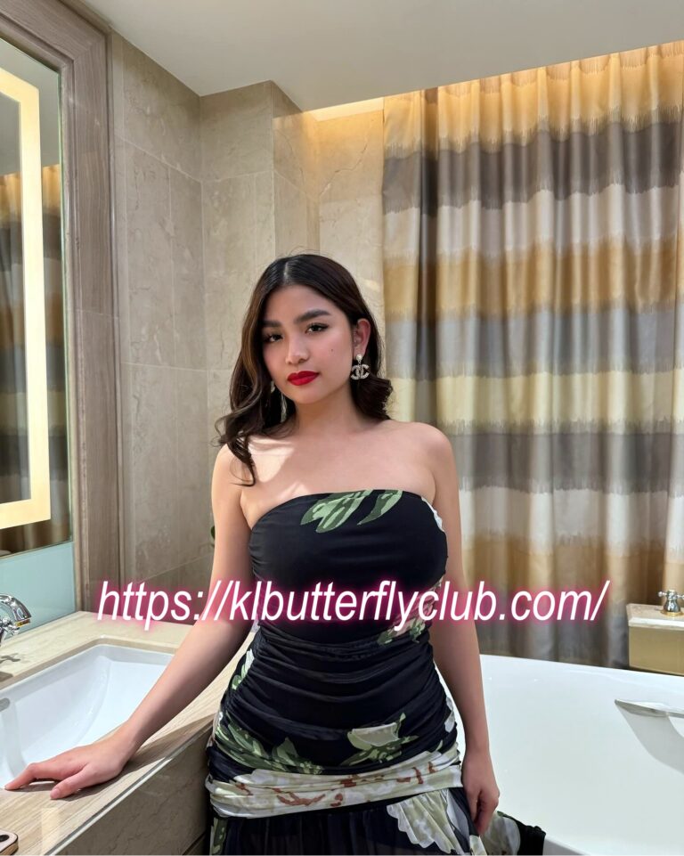 Woman in a strapless camouflage dress with red lipstick posing by a bathroom vanity and tub; watermark reads 'klbutterflyclub.com'.